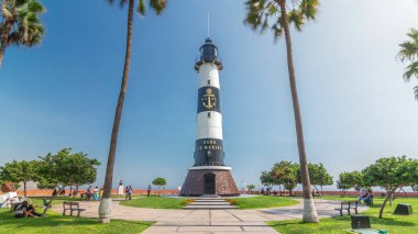 Miraflores Parkı 'ndaki deniz feneri manzaralı anıt zaman atlaması. Çiçekli ve palmiyeli yeşil çimenler. Güneşli bir günde sahil şeridi parkı. Lima, Peru