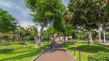 Miraflores Central Park zaman atlamalı yeşil ağaçlar ve Peru başkentindeki çimlerle dinlenmek için bir yer. İnsanlar banklarda oturup yürüyorlar. Lima, Peru