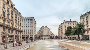 Fransa 'nın Lyon şehrindeki Place de la Republique' in hiperlapesi. Meydanda, tarihi binalarla çevrili büyük bir çeşme var ve insanlar banklarda oturuyor.
