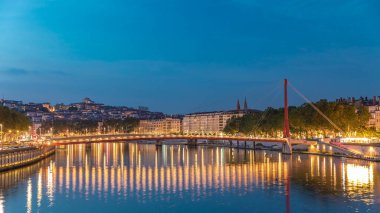 Lyon 'daki Saone Nehri' nin üzerindeki Palais du Justice Köprüsü 'nde, günden geceye geçiş. Rıhtımdaki aydınlık binalar gün batımından sonra suya yansıyor.