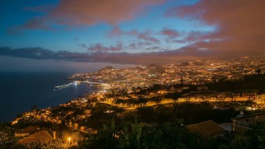 Gün batımından sonra adanın manzarası Funchal 'a gündüz, gece geçişi, Madeira, Portekiz zaman çizelgesi. Limanda akşam aydınlatması ve şehir ışıklarıyla