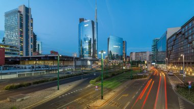 Günbatımından sonra Milano 'nun Milano kentinde, Porta Nuova iş bölgesindeki modern gökdelenleri ile birlikte gece ve gündüz geçiş panoramiklerini görüyoruz. Yollarda trafik vardı. Pencerelerde ışık var. Köprüden üst görünüm