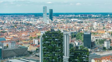 Milano 'nun modern kuleleri ve gökdelenleri iş bölgesinin zaman çizelgesinde balkonlarda ağaçlarla çevrili çatıdan görünüşü. Kırmızı çatılı evler. Yazın mavi bulutlu gökyüzü