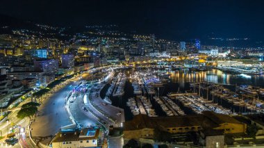 Monte Carlo 'nun Panorama' sı geceleyin Herkül Limanı ile Monako köyündeki gözlem güvertesinden hızla yükseliyor. Liman manzaralı, aydınlık binalar ve yatlar. Yolda trafik vardı.