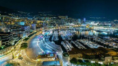 Monte Carlo 'lu Panorama, Monaco köyündeki gözlem güvertesinden Herkül Limanı ile birlikte. Aydınlatmalı binalar ve liman manzaralı yatlar. Yolda trafik vardı.