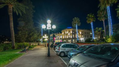 Sokakta gece yürüyüşü Beaulieu-sur-Mer 'in merkezinde palmiyeler hiperhızlandırılmış. Akşam gökyüzü. Kumarhane ve yakınlardaki binalar. Yolda trafik vardı.