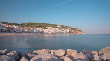 Sesimbra, Portekiz 'in küçük bir kasabasındaki iskeleden sahile, güneşli bir günde güneş batmadan önce mavi gökyüzü ile panorama zamanlaması hipervane