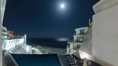 Sesimbra, Portekiz 'deki modern yüzme havuzlu otel binasının ay ışığıyla gece görüntüsü. Arka planda okyanus olan plaj