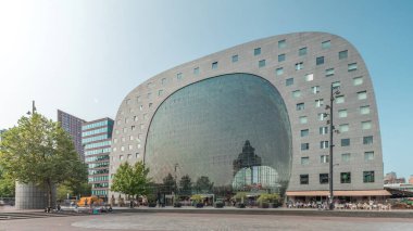 Rotterdamse Markthal 'ın dış yüzeyinde aşırı kayma. Dükkanları ve restoranları olan ikonik at nalı şeklinde bir bina. Meydanda gezinen insanlar. Gökdelenler ve arka planda canlı bir şehir manzarası