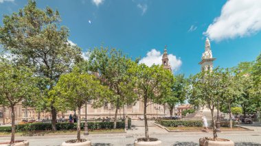Plaza del Triunfo zaman atlaması ve Sevilla Katedrali 'nin kusursuz gebelik anıtı. Yeşil ağaçlar, tarihi mimari, bulutlu mavi gökyüzü. Endülüs, İspanya 'da manzara