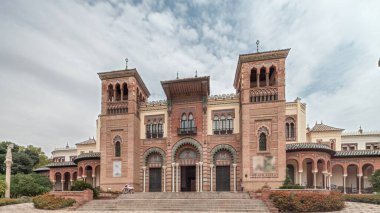 Maria Luisa Park 'taki Sevilla Sanat ve Gelenekler Müzesi cephesi. Plaza de America 'da Mudejar tarzı bir bina var. Bulutlu gökyüzü altında zaman atlaması. Sevilla, İspanya.