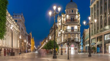 Avenida de la Constitucion, Seville, İspanya 'da günden geceye zaman dilimi. Iconic Adriatica binası gün batımından sonra parlıyor. Modern sokak lambaları, yayalar ve şehir atmosferine sahip tarihi mimari