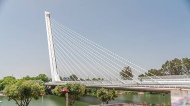 İspanya 'nın Sevilla kentindeki Guadalquivir Nehri' nin üzerinden geçen uzun kolon ve çelik kablolu Alamillo Köprüsü. Açık mavi gökyüzü altında yoğun trafik ile modern süspansiyon tasarımının hızlandırılmış zamanlaması.