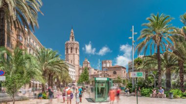Valencia, İspanya 'da Plaza de la Reina' nın panoramik zaman atlaması. Tarihi bir kilise kulesi, hareketli kafeler ve sıcak Akdeniz semaları altında palmiyeleri olan merkezi bir çeşme..