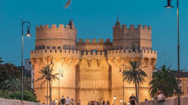 Serrans Towers (Torres de Serranos) İspanya 'nın Valencia şehrinde günden geceye geçiş zamanı. Şehrin antik duvarlarından gelen büyük bir ortaçağ kapısı. İnsanlar tarihi bir dönüm noktasının yakınındaki bir köprüde yürüyorlar.