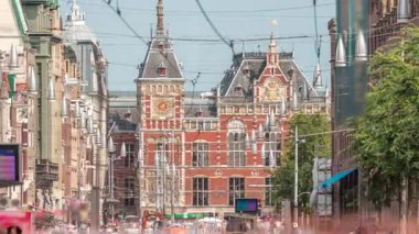 Damrak Caddesi, Dam Meydanı 'ndan Centraal İstasyonu' na giden, tramvaylı bir zaman diliminde. İnsanlar tramvay durağında beklerken trafik yolda ilerliyor. Amsterdam, Hollanda