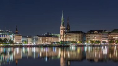 Binnenalster 'in Hamburg, Almanya' daki Belediye Binası ve Nikolai Kilisesi 'ndeki gece programı. Aydınlatılmış tarihi binalar yıldızlı bir gökyüzünün altındaki Alster Gölü sularına yansıyor. Manzaralı şehir manzarası
