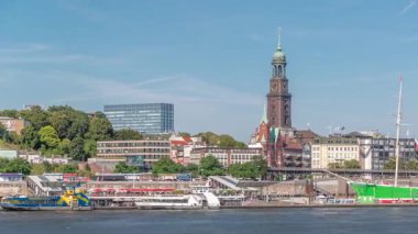 Elbe nehir kenarı ve Hamburg, Almanya 'daki St. Michaels kilise kulesinin panoramik zaman çizelgesi. İskeleye yakın teknelerle manzara, Jan Fedder gezinti güvertesi ve oradan geçen feribotlar. Nehir kenarındaki canlı şehir manzarası
