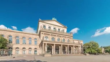 Hanover Devlet Operası Staatsoper Hannover ön görüntüsü. Şehir meydanında canlı mavi bulutlu bir zaman dilimi altında yürüyen insanların olduğu klasik tarzda bir tiyatro. Almanya