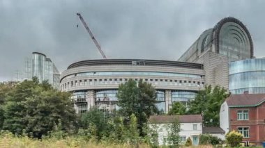 Brüksel 'deki Avrupa Mahallesi' ndeki binalar Avrupa Parlamentosu, Komisyon ve dramatik bulutlu gökyüzü altındaki kurumlarla aynı tarihe denk geliyor. Leopold Park ön planda kırmızı tuğlalı evle