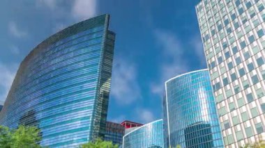 Modern ofis binalarının zaman çizelgesi. Parktaki yeşil ağaçlar tarafından çerçevelenmiş parlak mavi gökyüzü üzerinde yansımaları ve röfleleri olan cam gökdelenler. Brüksel, Belçika 'da güneş ışığı ve geçen bulutlar