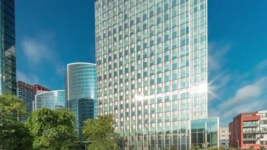 Panorama modern ofis binalarının zaman çizelgesini gösteriyor. Parktaki yeşil ağaçlar tarafından çerçevelenmiş parlak mavi gökyüzü üzerinde yansımaları ve röfleleri olan cam gökdelenler. Brüksel 'de güneş ışığı ve geçen bulutlar