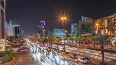 Riyad, Suudi Arabistan 'ın şehir havası gece zaman çizelgesi. Aydınlatılmış ünlü kuleler, gökdelenler, Kral Fahd Yolu ve yoğun trafik yer alıyor. Palmiyeler ve sokak lambaları şehrin içinden geçen ana otoyol boyunca uzanır.