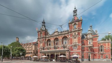 Uluslararası Amsterdam Tiyatrosu 'nun hiperlapası. Leidseplein' da yürüyen insanlar var. Tramvay dramatik bulutların altında tarihi binanın önünden geçiyor. Amsterdam, Hollanda