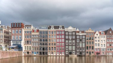 Damrak 'taki renkli Kanal Evleri' nin gece ışığında aşırı hızlanması dramatik bulutların altında geçen teknelerle suya yansıdı. Hollanda, Amsterdam 'ın büyüleyici manzarası