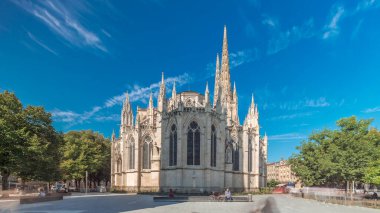 Saint-Andre de Bordeaux Katedrali. Mavi gökyüzünün altında ikiz kuleleri olan hızlandırılmış zaman atlaması. Yeşil ağaçlar ve meydanda yürüyen insanlar sakin bir şehir atmosferi yaratıyor. Bordeaux, Fransa