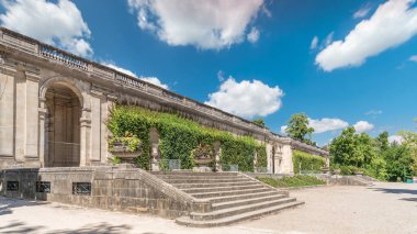 Fransa 'nın başkenti Jardin' de Palais du Capitole 'de zaman atlaması. Sarmaşık kaplı yeşil ağaçlar, merdivenler ve parlak mavi bulutlu gökyüzü ile çevrili tarihi bir binanın manzarası.