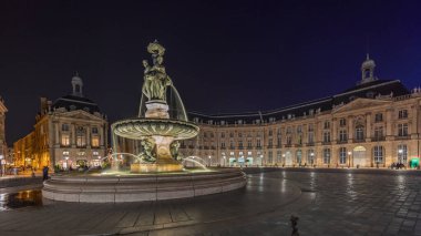 Panorama, Place de la Bourse 'u ve Fransa' nın Bordeaux şehrindeki çeşmeleri gösteriyor. Aydınlatılmış tarihi binalar büyük meydanın sınırında. Trafik ve sokakta hareket sahneyi güçlendirir