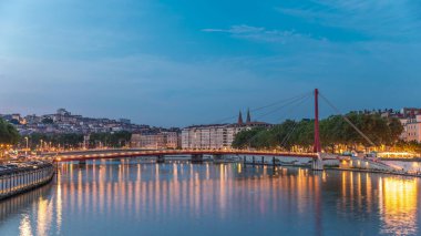 Lyon 'daki Saone Nehri' nin üzerindeki Palais du Justice Köprüsü 'nde, günden geceye geçiş. Rıhtımdaki aydınlık binalar gün batımından sonra suya yansıyor.