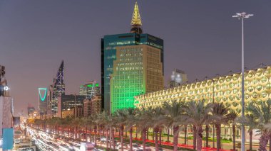 Suudi Arabistan, Riyad 'daki Kral Fahd Yolu' nun hava-gece zaman çizelgesi. Aydınlatılmış Riyad Ulusal Kütüphanesi yakınlarında modern kuleler ve gökdelenlerle çevrili araçlar ve taksilerle dolu.