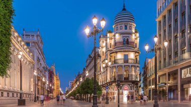 Avenida de la Constitucion, Seville, İspanya 'da günden geceye zaman dilimi. Iconic Adriatica binası gün batımından sonra parlıyor. Modern sokak lambaları, yayalar ve şehir atmosferine sahip tarihi mimari