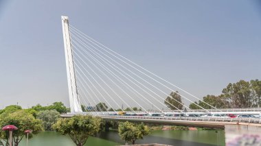 İspanya 'nın Sevilla kentindeki Guadalquivir Nehri' nin üzerinden geçen uzun kolon ve çelik kablolu Alamillo Köprüsü. Açık mavi gökyüzü altında yoğun trafik ile modern süspansiyon tasarımının hızlandırılmış zamanlaması.