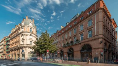 Toulouse, Occitanie, Fransa 'da Rue de Metz' in zaman çizelgesini gösteren panorama, tarihi cepheleri, dükkanları, kafeleri, trafiği ve mavi bulutlu gökyüzünü gösteriyor. Şehrin göbeğinde canlı bir şehir manzarası