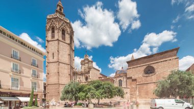 Valencia, İspanya 'da Plaza de la Reina' nın panoramik zaman atlaması. Tarihi bir kilise kulesi, hareketli kafeler ve sıcak Akdeniz mavi bulutlu gökyüzünün altında merkezi bir çeşme ile dolu canlı bir meydan..