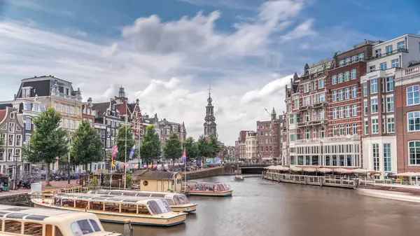 Amstel Nehri, rıhtım ve Munttoren kulesinin yer aldığı Amsterdam şehir merkezinin panoramik zaman atlaması. Tekneler bulutlu gökyüzünün altında ileri geri yüzerler. Köprüden manzaralı şehir manzarası. Hollanda