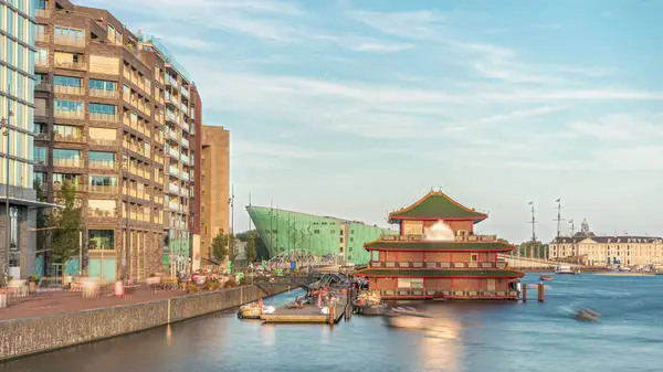 Sudaki pagoda şeklinde bir Çin restoranının hipervanesi, tarihi şehir merkezi binalarının ve günbatımında modern mimarinin arka planına karşı kurulur. Amsterdam, Hollanda