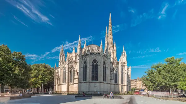 Saint-Andre de Bordeaux Katedrali. Mavi gökyüzünün altında ikiz kuleleri olan hızlandırılmış zaman atlaması. Yeşil ağaçlar ve meydanda yürüyen insanlar sakin bir şehir atmosferi yaratıyor. Bordeaux, Fransa