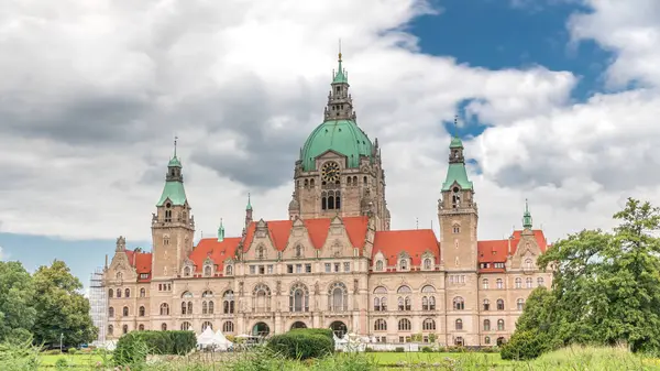 Hanover 'in Yeni Belediye Binası' nın hiperlapesi. Bulutlu bir gökyüzünün altında park ve göl ile çevrili tarihi bir kale gibi bir yapı. Su ve yeşillik üzerindeki yansımalar bu ikonik şehir manzarası zaman çizelgesini oluşturuyor. Almanya