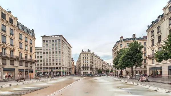 Fransa 'nın Lyon şehrindeki Place de la Republique' in hiperlapesi. Meydanda, tarihi binalarla çevrili büyük bir çeşme var ve insanlar banklarda oturuyor.