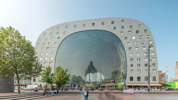 Rotterdamse Markthal 'ın dış yüzeyinde aşırı kayma. Dükkanları ve restoranları olan ikonik at nalı şeklinde bir bina. Meydanda gezinen insanlar. Gökdelenler ve arka planda canlı bir şehir manzarası