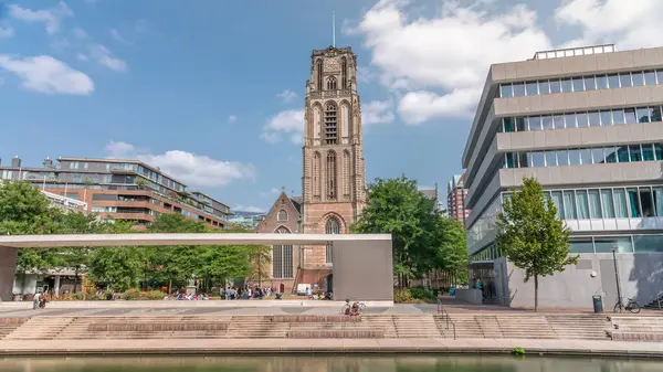Laurenskerk 'in (Saint Lawrence Kilisesi) Grotekerkplein, Rotterdam' daki hiperlapesi. İnsanlar mavi bulutlu gökyüzünün altında çimlerde dinleniyorlar. Kanal merdivenlerinin yanında saati olan tarihi çan kulesi. Hollanda