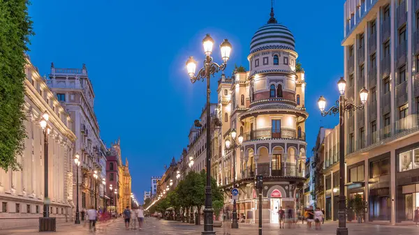 Avenida de la Constitucion, Seville, İspanya 'da günden geceye zaman dilimi. Iconic Adriatica binası gün batımından sonra parlıyor. Modern sokak lambaları, yayalar ve şehir atmosferine sahip tarihi mimari