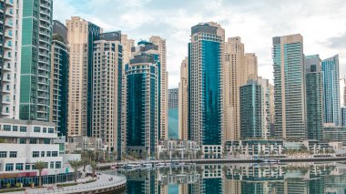 Dubai Marina 'daki köprüden sabah görüntüsü su ve gezinti saatlerine yansıyan modern kuleler Birleşik Arap Emirlikleri. Yapay kanalı olan bir bölge. Mavi bulutlu gökyüzü