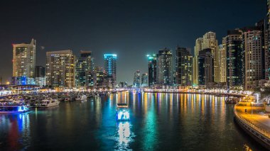 Dubai Limanı 'ndaki köprüden gece görüşü yanıp sönen ışıklarla aydınlanan kuleler yüzen yatlar ve botlarla suya yansıyordu Birleşik Arap Emirlikleri. Dubai bölgesi ve yapay bir kanal.