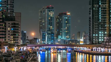 Gece Dubai Marina 'da gezinti zamanı, BAE. Palmiyeler, yüzen tekneler ve konut kuleleri ile rıhtım manzarası. Dubai 'de yapay kanallı bir bölge.