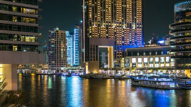 Dubai Marina rıhtımı, yatları ve Dubai 'deki köprüden modern kuleleri olan gece zaman çizelgesi, Birleşik Arap Emirlikleri. Avuçlar ve kafeler